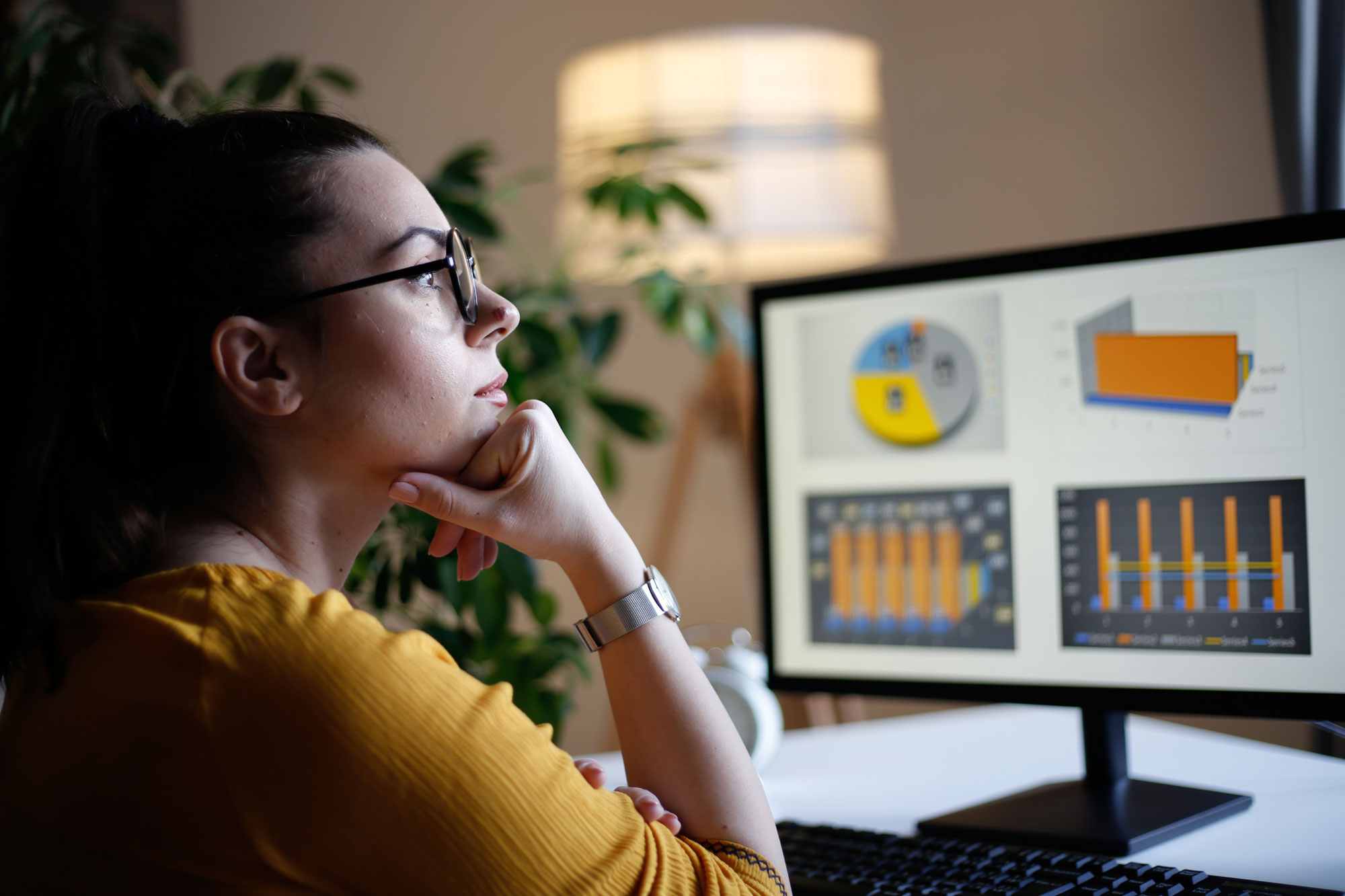 woman sitting at a desk with her fist under her chin staring at reporting software & graphs